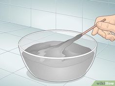 a bowl filled with gray liquid and a spoon in it's hand, sitting on a tiled floor