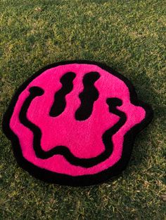 a black and pink rug with a smiley face drawn on it sitting in the grass