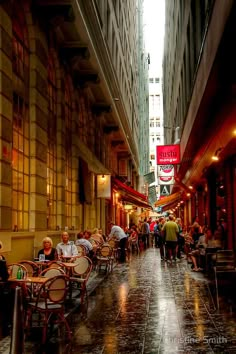 people are sitting at tables in the middle of an alleyway on a rainy day