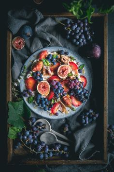 a white plate topped with fruit on top of a wooden table next to grapes and figs