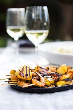 grilled pineapple and shrimp skewers on a plate with wine glasses in the background