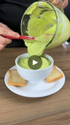 a person pouring guacamole into a bowl with toasted bread on the side