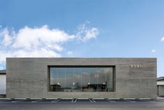 an empty parking lot in front of a building with glass windows on the side and sky behind it