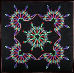 a black quilt with multicolored flowers and leaves in the center, on top of a wooden frame