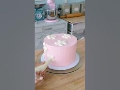 a woman is decorating a pink cake with white flowers on the top and bottom