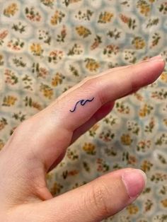 a person's finger with a small wave tattoo on the tip of their thumb