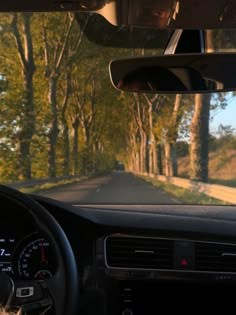 the inside view of a car driving down a road with trees on both sides of it