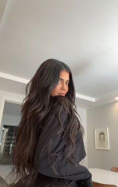 a woman with long dark hair standing in a living room next to a dining room table