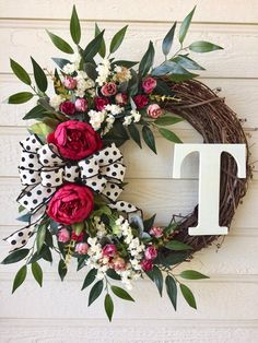 a floral wreath with the letter t is hanging on a white wall next to a door