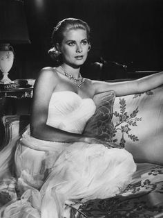 a black and white photo of a woman in a dress sitting on a couch with her legs crossed