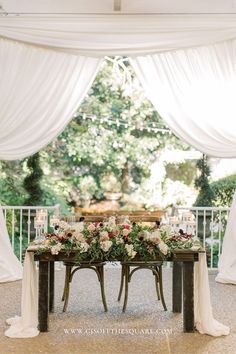 a table with flowers and candles on it in front of a white curtained area