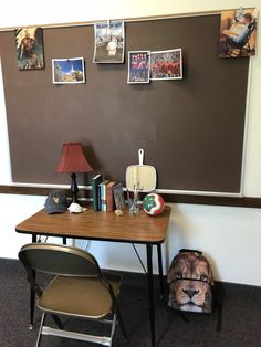 a desk and chair in front of a chalkboard with pictures on the wall behind it