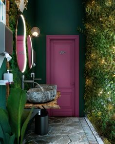 a bathroom with green walls and pink door next to a plant covered wall in the corner