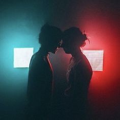 two people standing next to each other in front of a red and green light on a wall