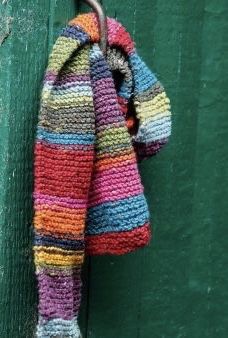 a multicolored scarf hanging from a hook on a green door