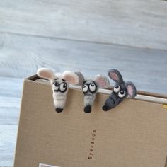 three small stuffed animals in a cardboard box on a wooden table, one is peeking out from behind the other