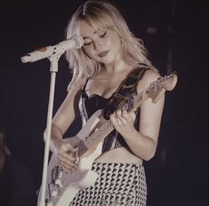 a woman holding a guitar while standing in front of a microphone