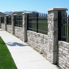 a row of stone fences next to a sidewalk with grass and mountains in the background