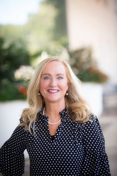 a woman with blonde hair wearing a black and white polka dot blouse smiling at the camera