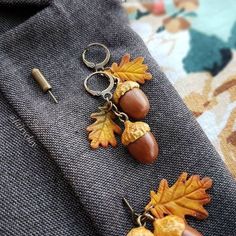 a pair of acorns and leaves are hanging from a tie clip on a piece of fabric