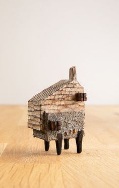 a small toy house made out of wood on a wooden table with a white wall in the background