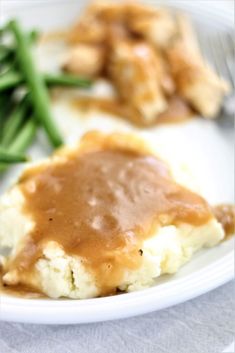 mashed potatoes with gravy and green beans on a white plate, ready to be eaten