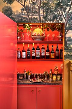 a red cabinet filled with lots of bottles and glasses next to a painting on the wall