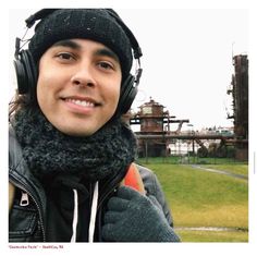 a man wearing headphones and a black jacket in front of an industrial park area