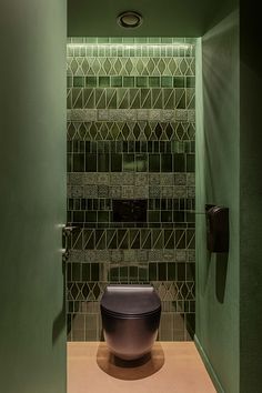 a green bathroom with a black toilet in the corner and tiled wall behind it,