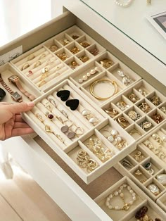 a drawer filled with lots of jewelry on top of a white table next to a window