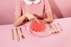 a woman sitting at a pink table with utensils and a glass bowl in front of her