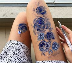 a woman's legs with blue flowers on them and a pen in her hand