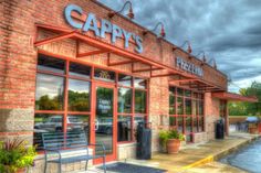 the front of a restaurant with an empty bench in front of it and cloudy skies above