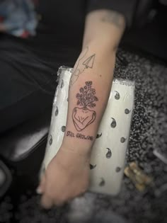 a person with a small tattoo on their arm holding a flower and heart shaped vase