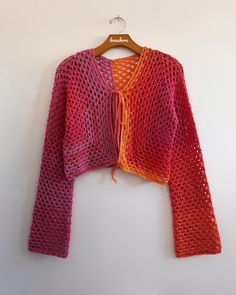 an orange and pink knitted jacket hanging on a white wall next to a wooden hanger