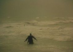 a man wading in the ocean on a foggy day