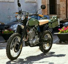 a dirt bike parked in front of a building with flowers on the ground and cars behind it