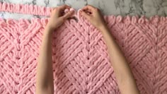 someone is crocheting the edge of a pink blanket with their hands on it