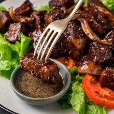 a fork is stuck into some meat on a plate with lettuce and tomatoes