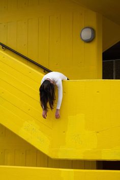 a woman leaning on a yellow wall with her head in the air and hands behind her back