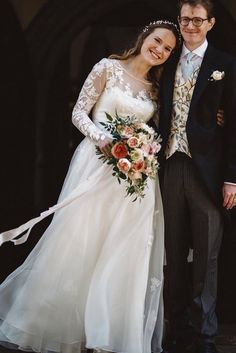 a bride and groom standing together in front of a building with flowers on the bouquet