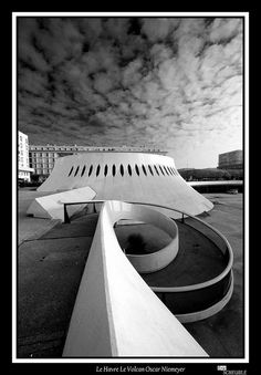 black and white photograph of an architectural structure in the middle of a parking lot with clouds overhead