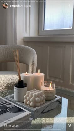 candles are sitting on a glass table in front of a chair with a white blanket