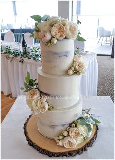 a three tiered wedding cake with flowers on the top and side is sitting on a wooden slice