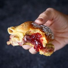 a hand holding a half eaten pastry with jelly on it