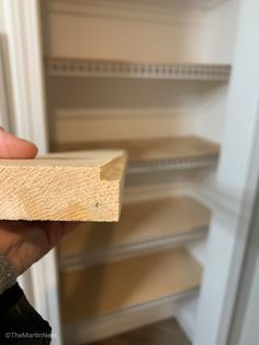 a hand holding a piece of wood in front of a refrigerator