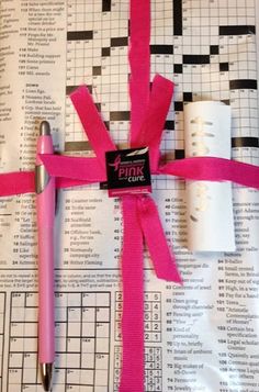 a pink ribbon tied to a cross on top of a newspaper with a pen in it