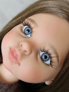 a doll with long hair and blue eyes is laying on a brown blanket looking at the camera