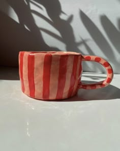 a red and white striped cup sitting on top of a table next to a shadow