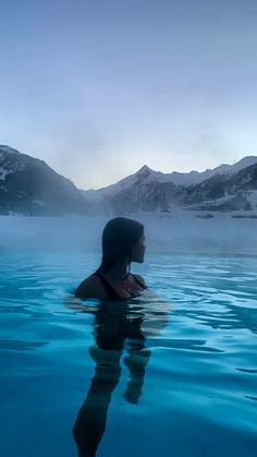 a person swimming in the water with mountains in the backgroung and foggy sky